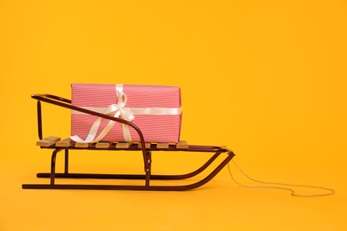 Stylish sleigh with Christmas gift on yellow background, space for text