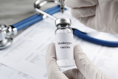 Nurse filling syringe with monkeypox vaccine from vial over table, closeup. Space for text