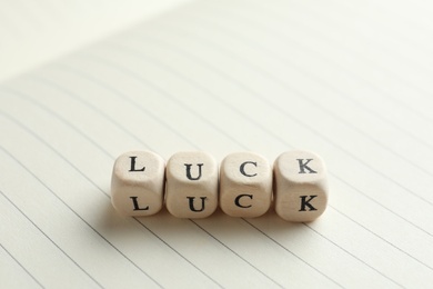 Word LUCK made with wooden cubes on open notebook, closeup