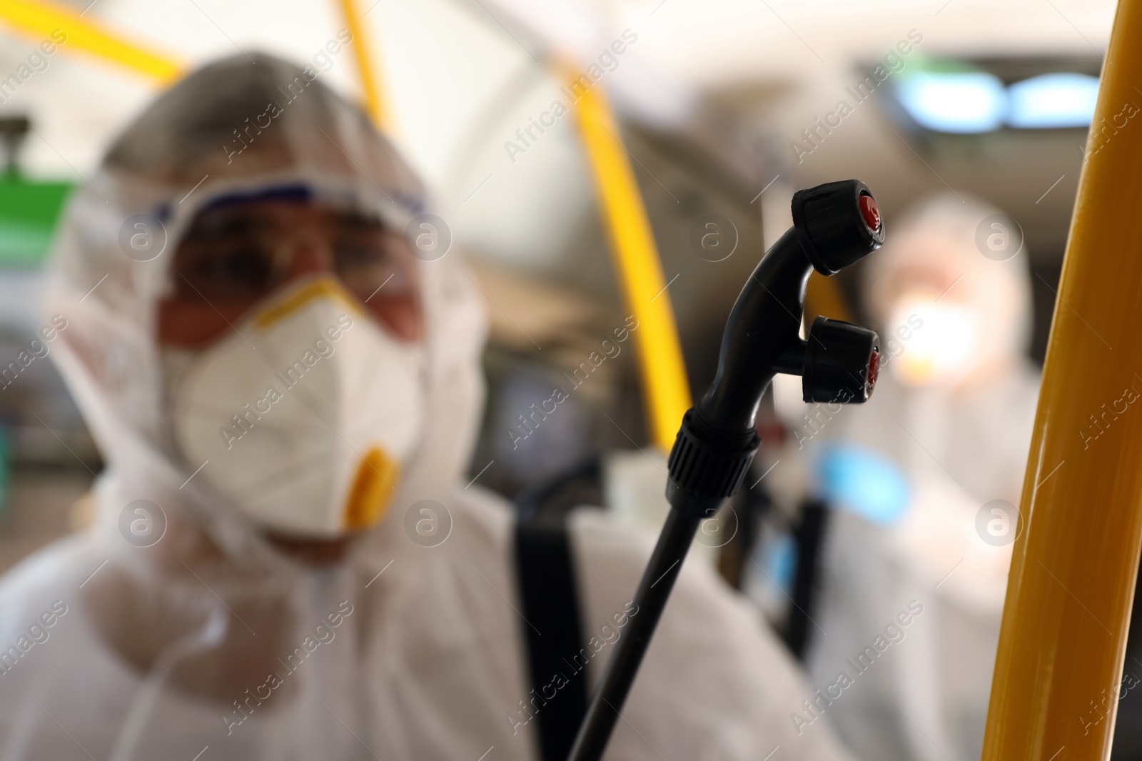 Photo of Public transport sanitation. Worker in protective suit disinfecting bus salon, focus on spray machine nozzle