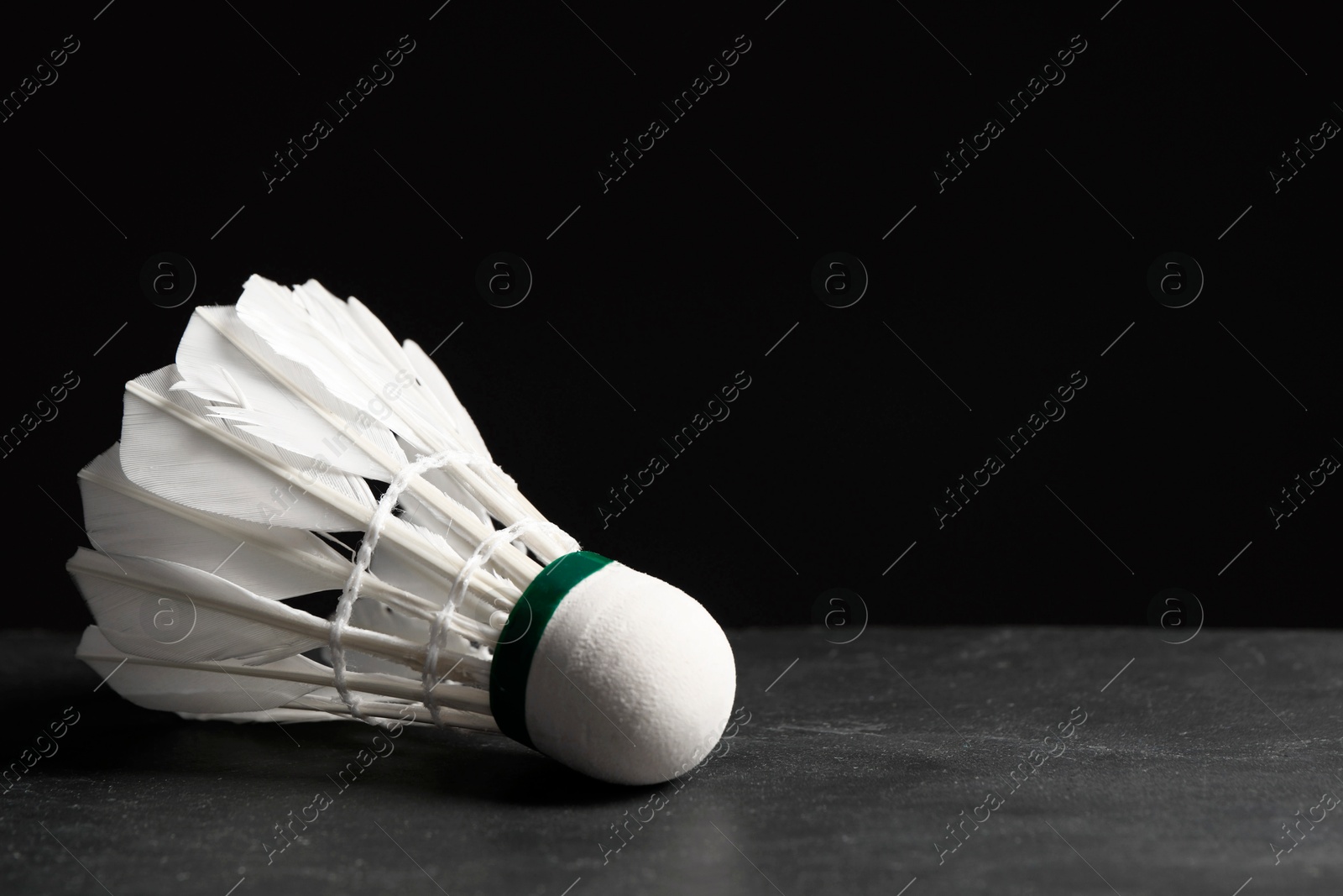 Photo of Feather badminton shuttlecock on grey table against black background, closeup. Space for text