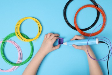 Photo of Boy drawing with stylish 3D pen on light blue background, top view