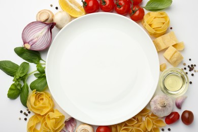 Photo of Plate surrounded by different types of pasta, products and peppercorns on white background, flat lay. Space for text