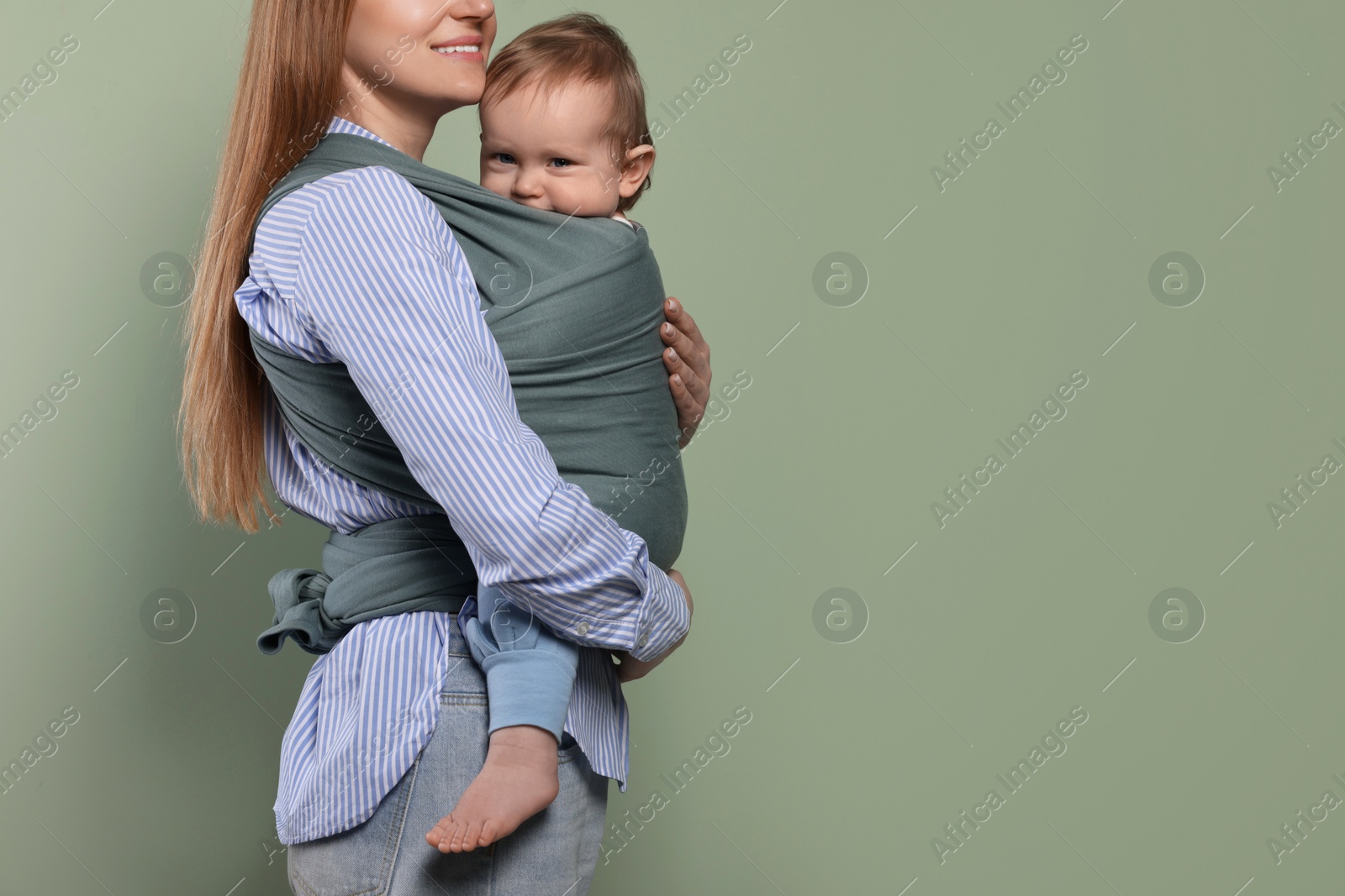 Photo of Mother holding her child in baby wrap on olive background, closeup. Space for text