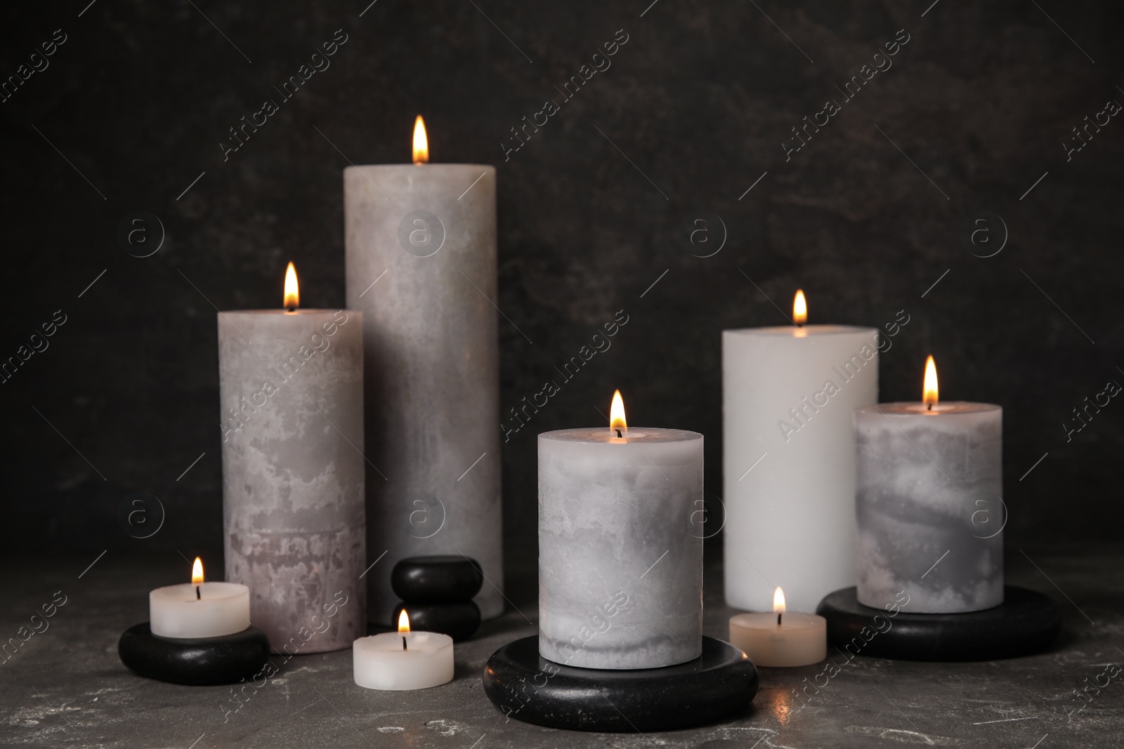 Photo of Burning candles and black spa stones on grey table