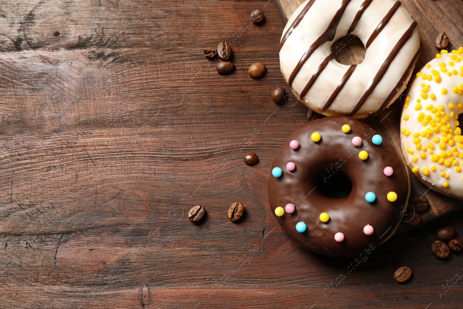 Photo of Yummy donuts with colorful sprinkles on wooden table, flat lay. Space for text