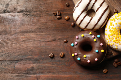 Photo of Yummy donuts with colorful sprinkles on wooden table, flat lay. Space for text