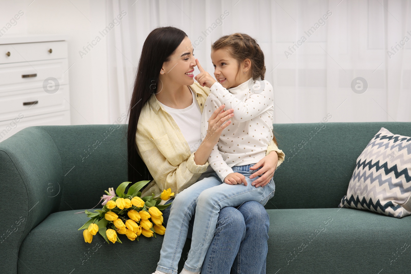 Photo of Happy woman and her cute daughter with bouquet of yellow tulips on sofa at home. Mother's day celebration