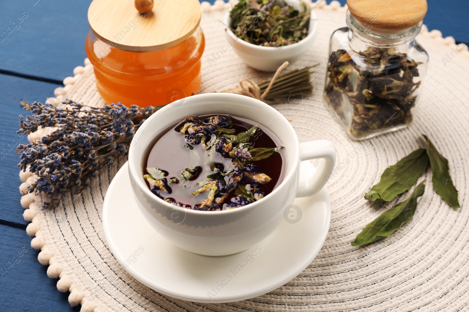 Photo of Aromatic tea with different dry herbs and honey on blue wooden table, closeup