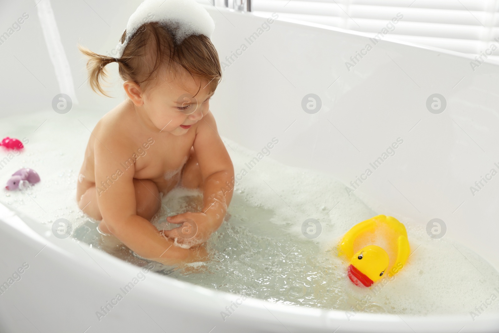 Photo of Cute little girl taking bubble bath with toys indoors. Space for text