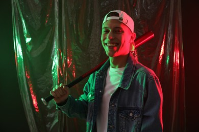 Young man with baseball bat on dark background in neon lights