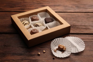 Photo of Candy paper cups near partially empty box of chocolate sweets on wooden table