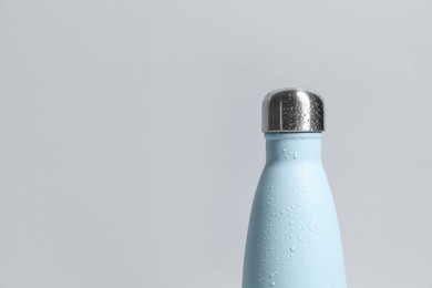 Photo of Stylish closed thermo bottle with water drops on light grey background, closeup. Space for text