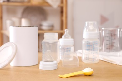 Photo of Scoop with powdered infant formula, can and bottles on wooden table indoors. Baby milk