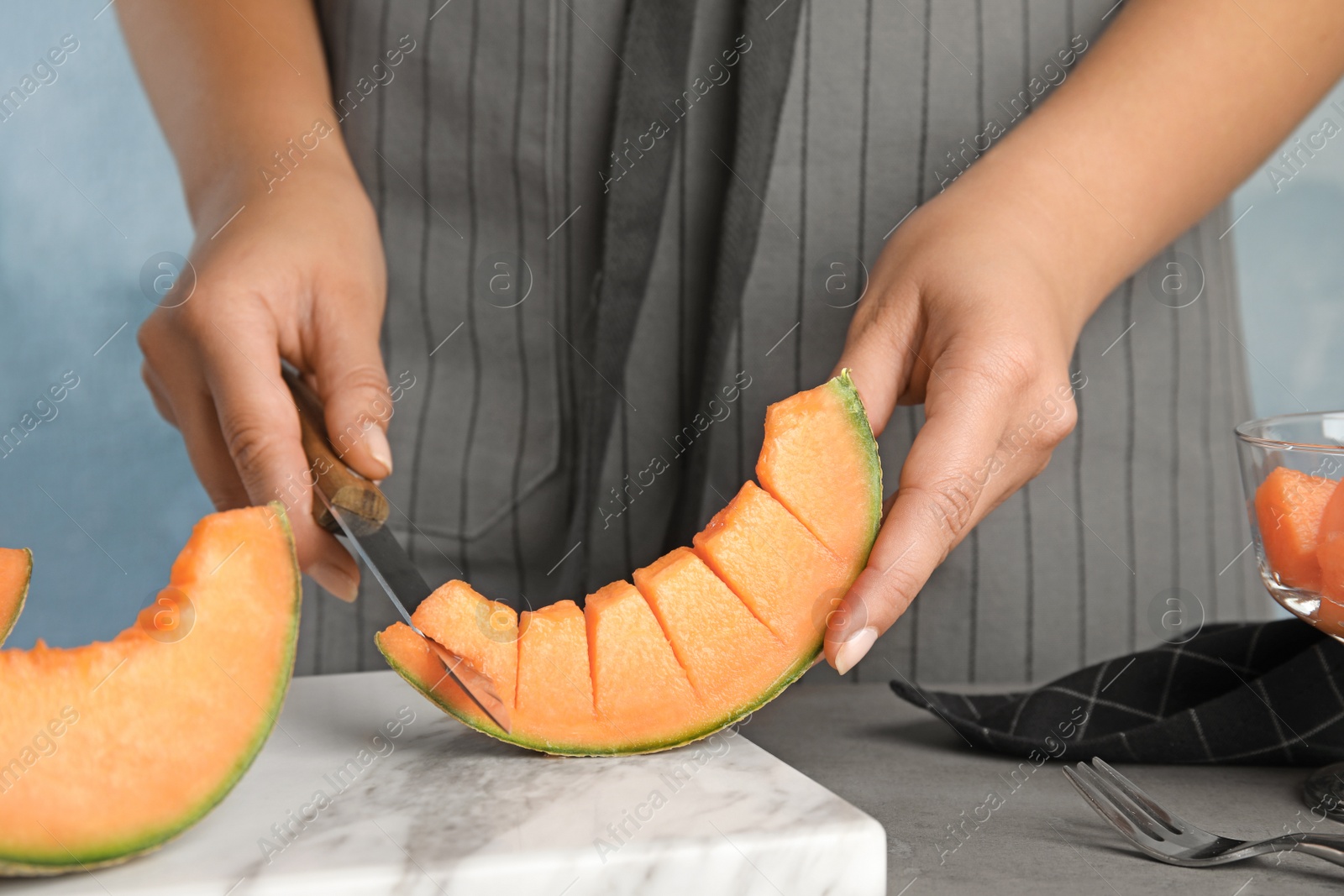 Photo of Young woman cutting cantaloupe melon slice at table, closeup
