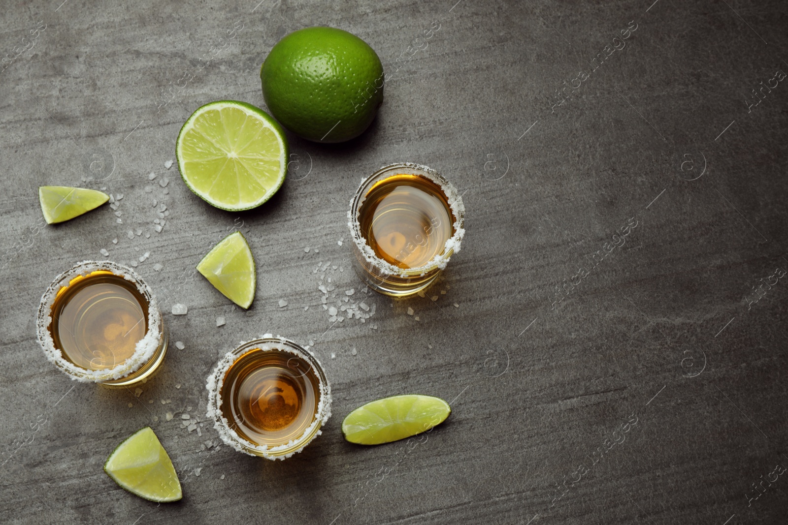 Photo of Mexican Tequila shots, lime slices and salt on grey table, flat lay. Space for text