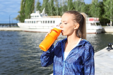 Photo of Woman in sportswear drinking protein shake near river