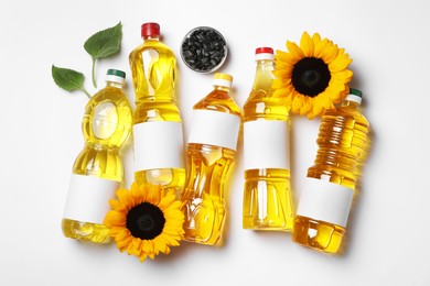 Photo of Bottles of sunflower cooking oil, seeds and beautiful flowers on white background, flat lay