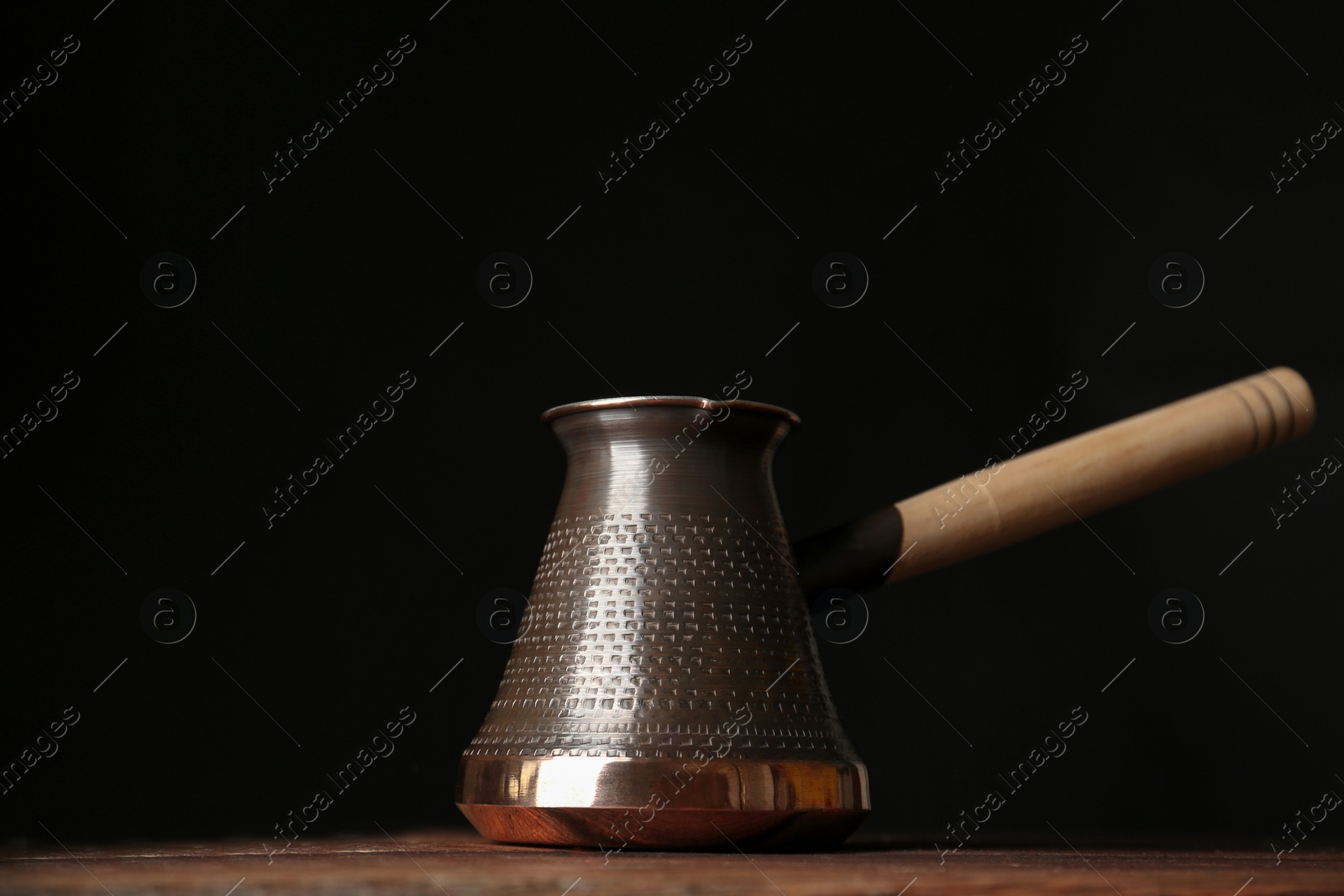 Photo of Beautiful copper turkish coffee pot on wooden table against dark background