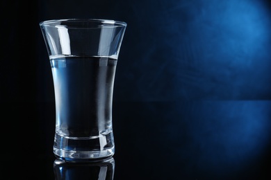 Shot glass of vodka on dark background with blue light. Space for text