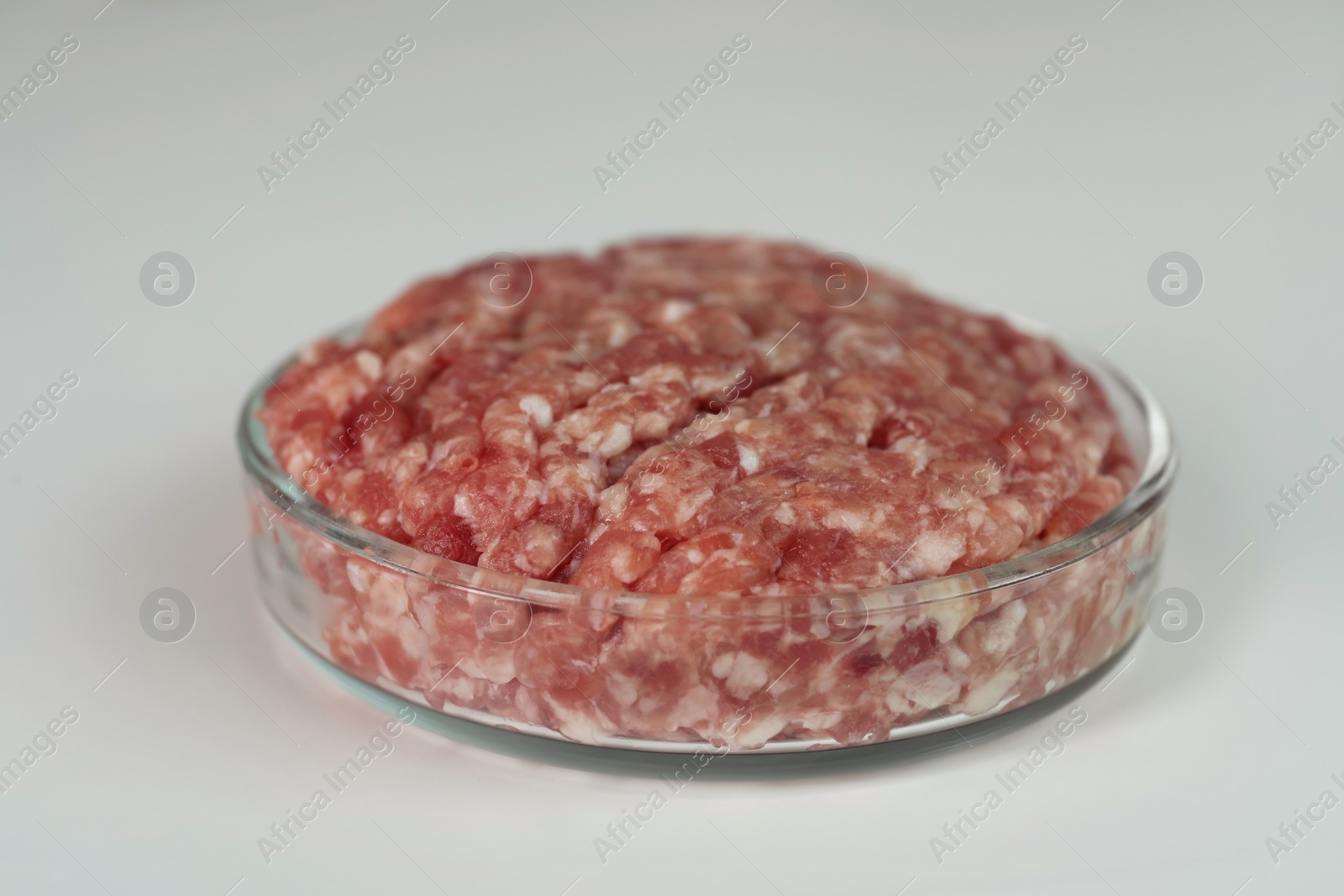 Photo of Petri dish with raw minced cultured meat on white table, closeup