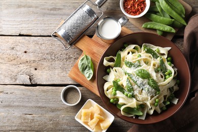 Photo of Delicious pasta with green peas and ingredients on wooden table, flat lay. Space for text