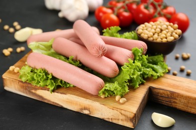 Photo of Fresh raw vegetarian sausages and vegetables on black table, closeup