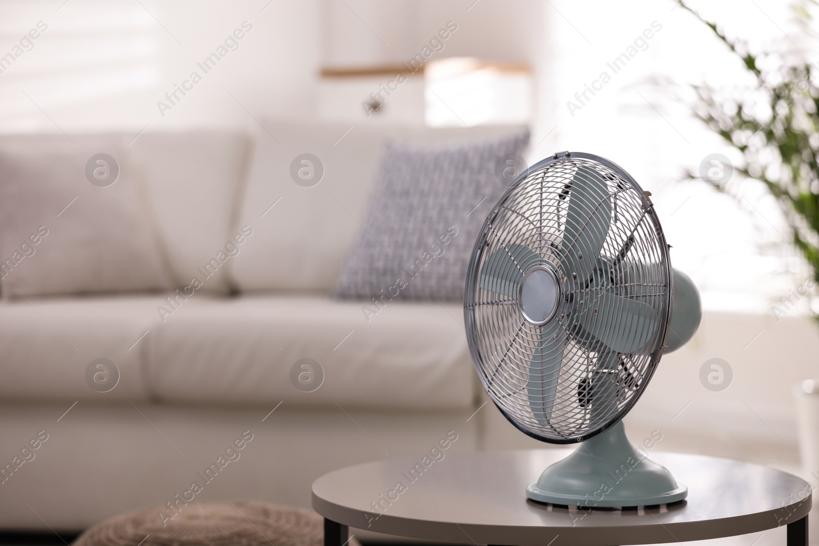 Photo of Modern electric fan on white table in living room. Space for text