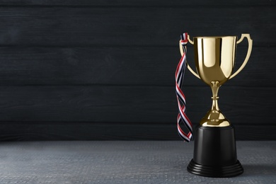 Photo of Golden trophy cup with ribbon on table against black wooden background. Space for text