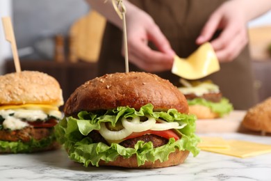 Woman making delicious vegetarian burger at white marble table, selective focus