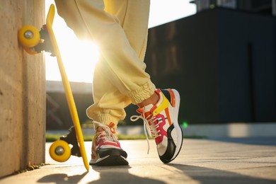 Photo of Woman with skateboard wearing stylish sneakers outdoors, closeup