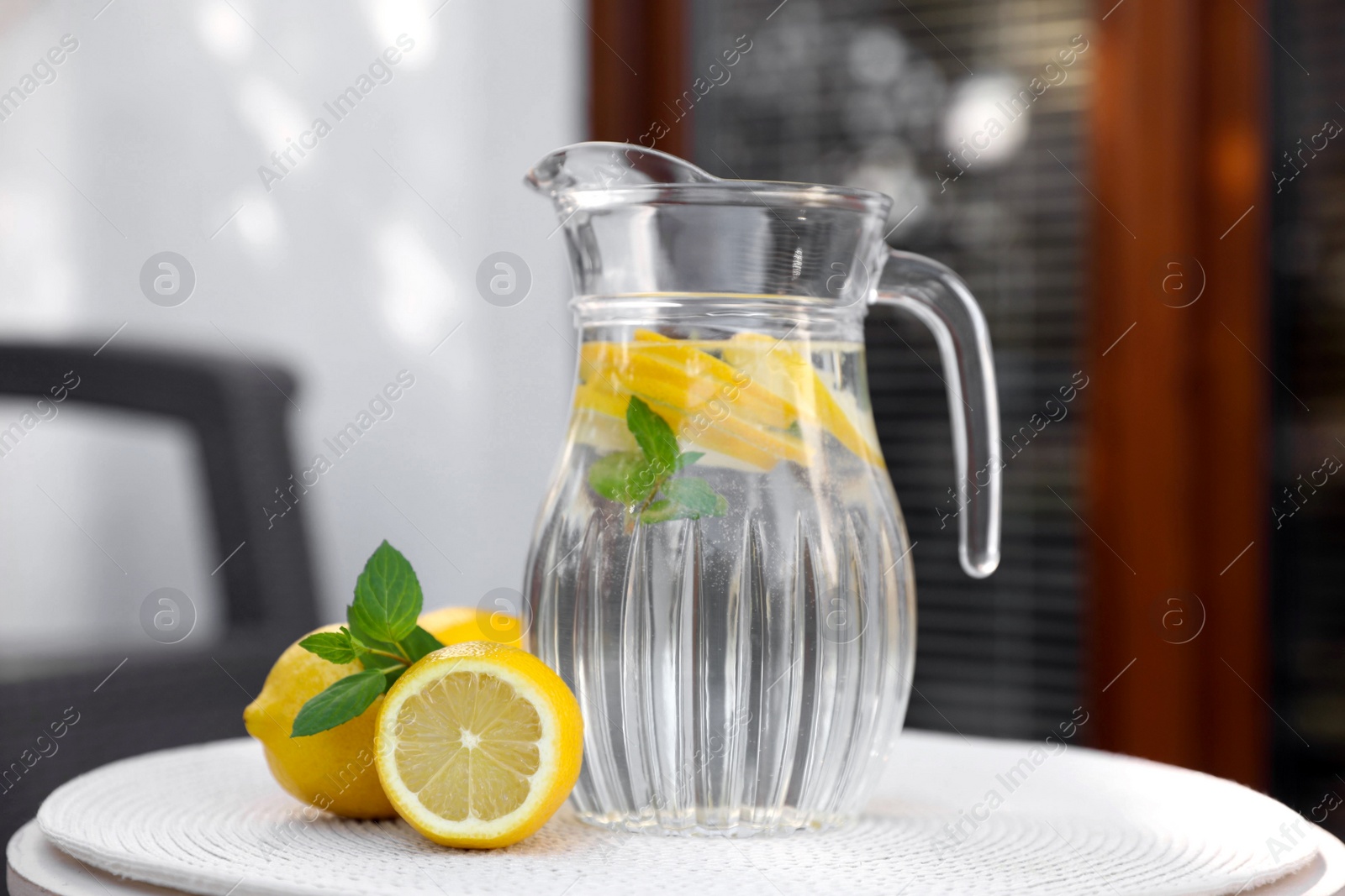 Photo of Jug of water with lemons and mint on white table outdoors