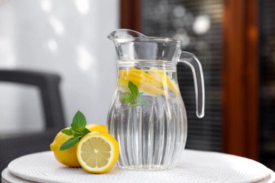 Jug of water with lemons and mint on white table outdoors