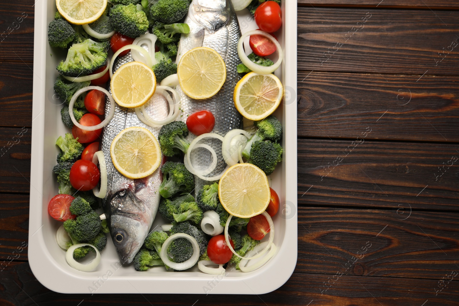 Photo of Raw fish with vegetables and lemon in baking dish on wooden table, top view. Space for text