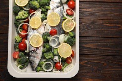 Photo of Raw fish with vegetables and lemon in baking dish on wooden table, top view. Space for text