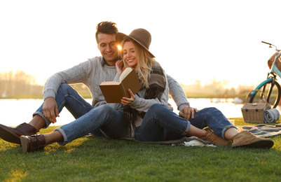Photo of Happy young couple reading book while having picnic outdoors