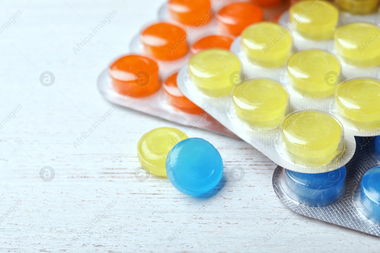 Photo of Blisters with color cough drops on white wooden background