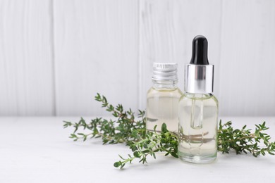 Photo of Bottles of thyme essential oil and fresh plant on white wooden table, space for text