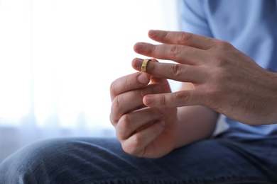 Photo of Man taking off wedding ring on blurred background, closeup. Divorce concept