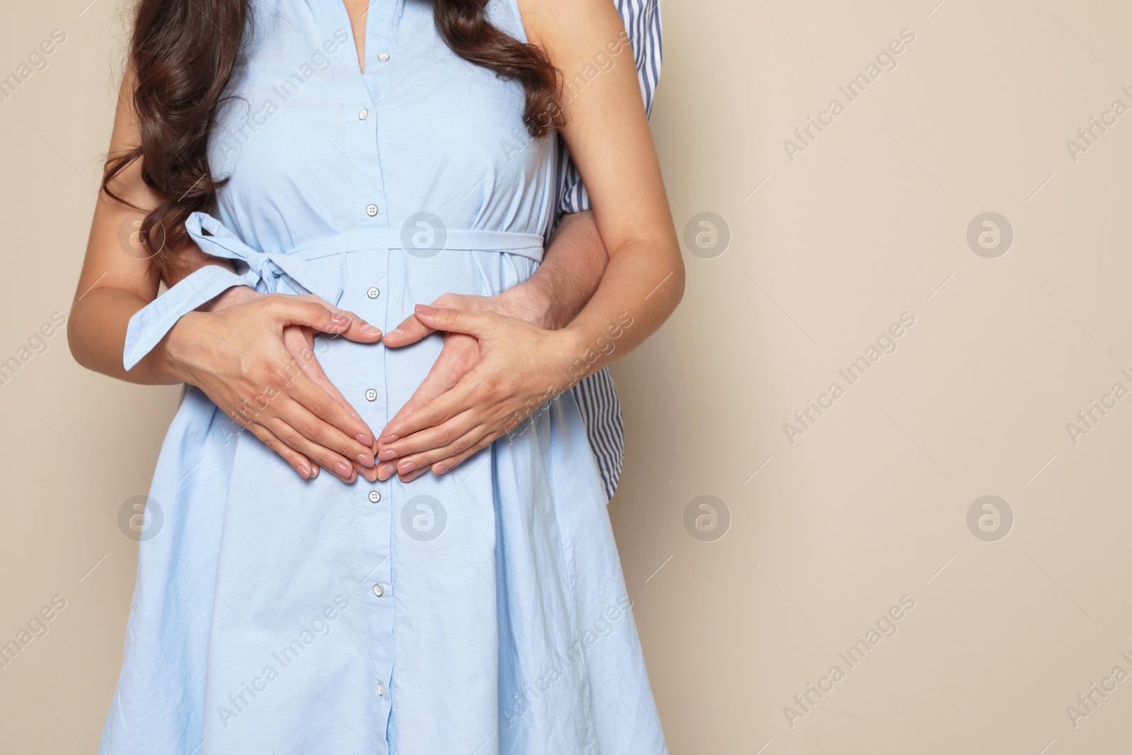 Photo of Husband and his pregnant wife showing heart with hands on color background, closeup. Space for text