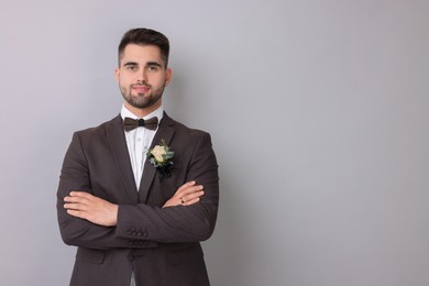 Handsome young groom with boutonniere on light grey background, space for text. Wedding accessory