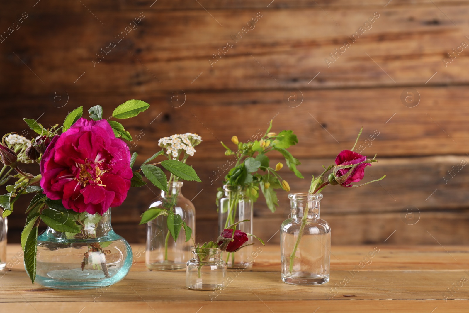 Photo of Different flowers in glass bottles on wooden table