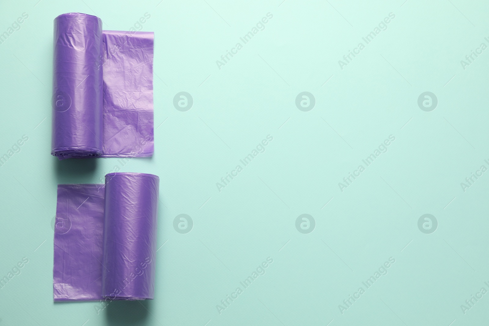 Photo of Rolls of violet garbage bags on turquoise background, flat lay. Space for text