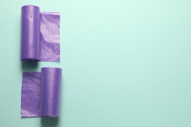 Rolls of violet garbage bags on turquoise background, flat lay. Space for text