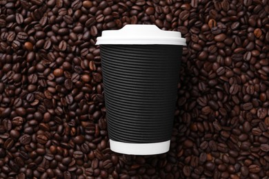 Photo of Coffee to go. Paper cup on roasted beans, top view