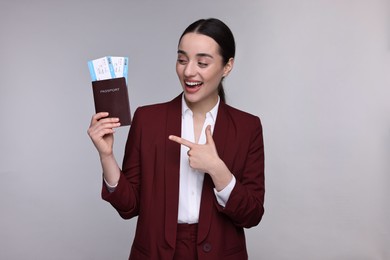 Photo of Happy businesswoman pointing at passport and tickets on grey background