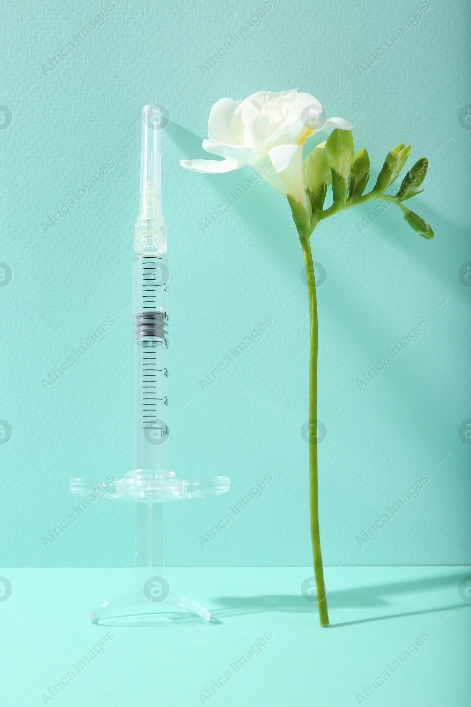 Photo of Cosmetology. Medical syringe and freesia flower on turquoise background