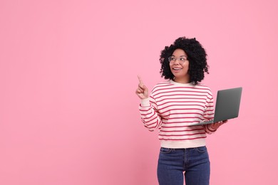 Photo of Happy young woman with laptop pointing at something on pink background. Space for text