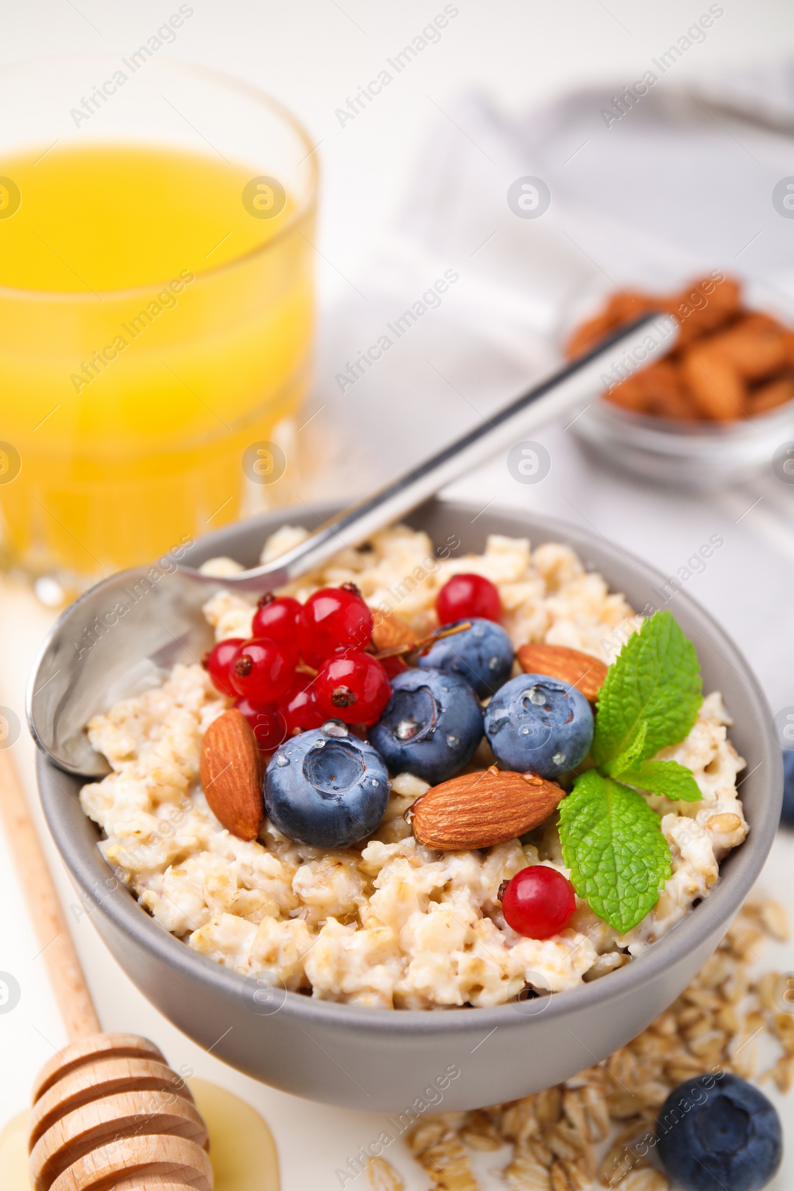 Photo of Oatmeal served with berries. almonds and mint on white table, above view