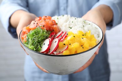 Photo of Woman holding delicious poke bowl with salmon and vegetables, closeup